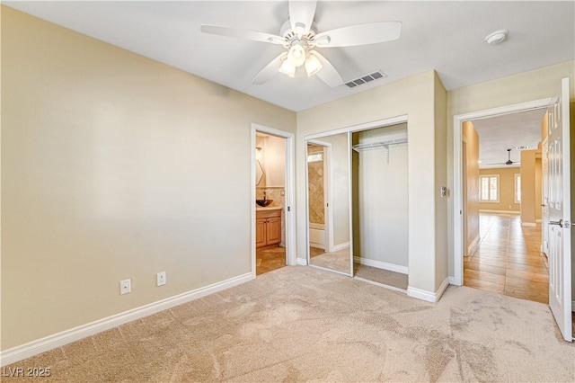 unfurnished bedroom with ceiling fan, light colored carpet, ensuite bathroom, and a closet