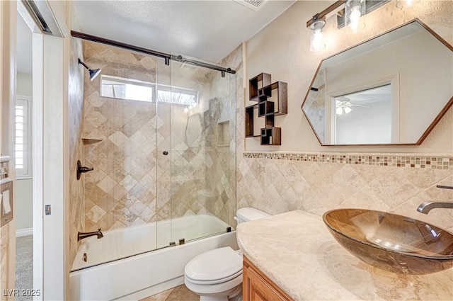 full bathroom with combined bath / shower with glass door, tile walls, vanity, tile patterned floors, and toilet