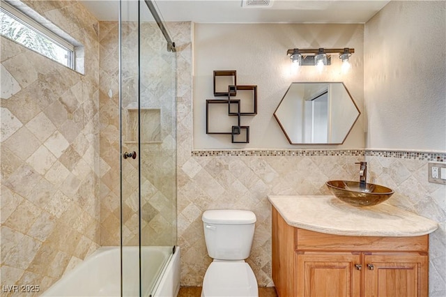 full bathroom with vanity, tile walls, shower / bath combination with glass door, and toilet