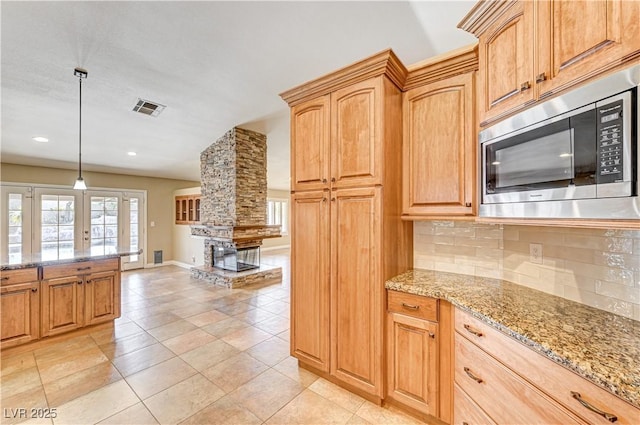 kitchen featuring light stone counters, stainless steel microwave, tasteful backsplash, and hanging light fixtures