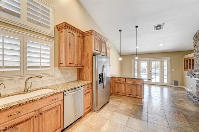 kitchen with sink, hanging light fixtures, light stone counters, stainless steel appliances, and french doors