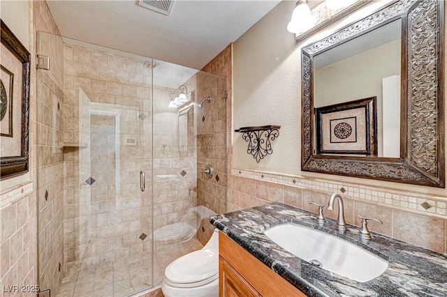 bathroom with walk in shower, toilet, tile walls, a textured ceiling, and vanity