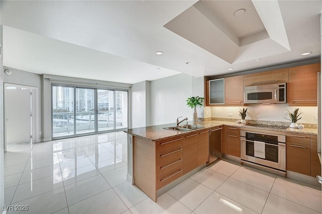 kitchen featuring sink, stone counters, appliances with stainless steel finishes, light tile patterned flooring, and kitchen peninsula