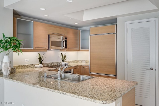 kitchen featuring sink, paneled built in fridge, light stone countertops, and kitchen peninsula