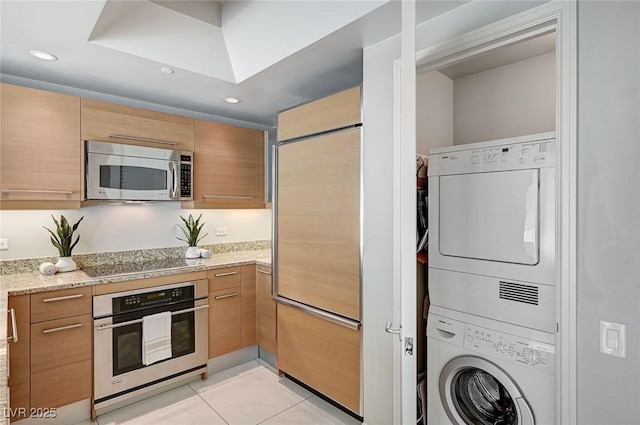 kitchen with stacked washer / dryer, light tile patterned flooring, appliances with stainless steel finishes, and light stone counters