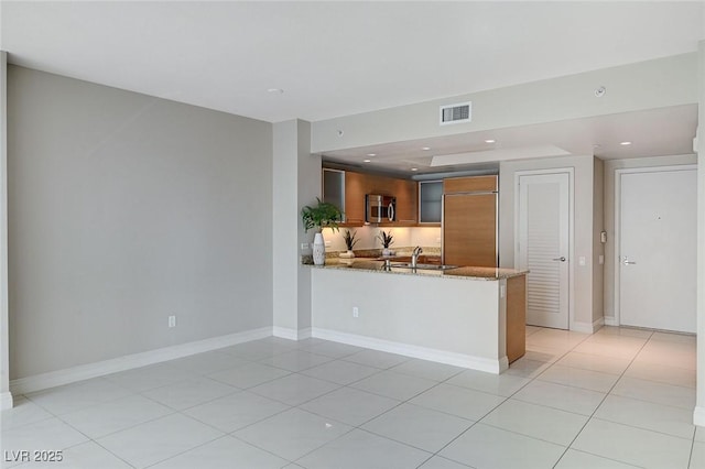 kitchen with sink, light tile patterned floors, paneled built in refrigerator, light stone countertops, and kitchen peninsula