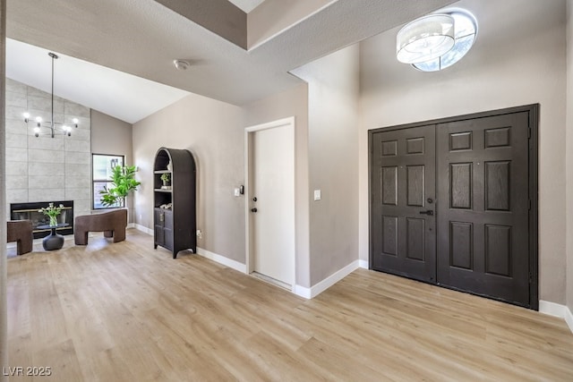 entrance foyer with lofted ceiling, a tiled fireplace, light hardwood / wood-style flooring, and an inviting chandelier