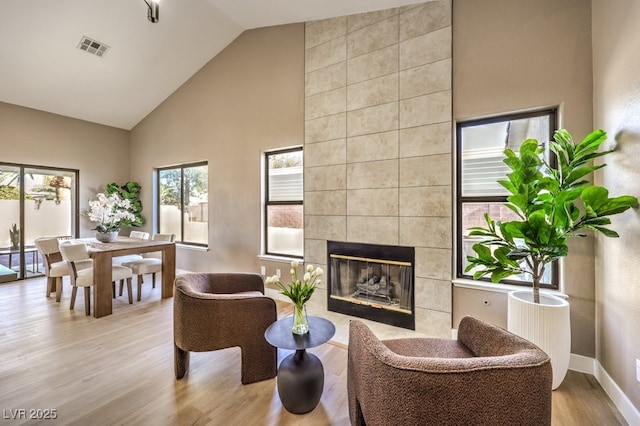 living room featuring a tiled fireplace, high vaulted ceiling, and light hardwood / wood-style floors