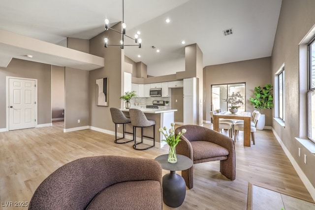 living room with a notable chandelier, high vaulted ceiling, and light hardwood / wood-style flooring