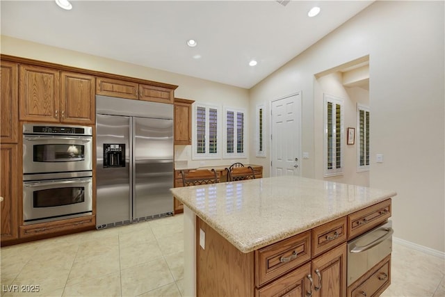 kitchen with light tile patterned flooring, appliances with stainless steel finishes, a center island, and light stone countertops