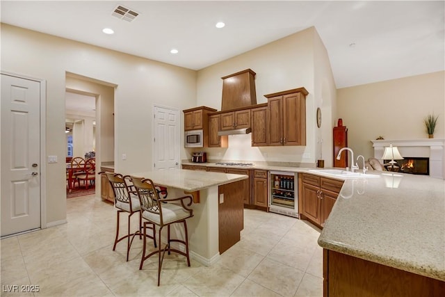 kitchen featuring sink, appliances with stainless steel finishes, wine cooler, light stone countertops, and kitchen peninsula