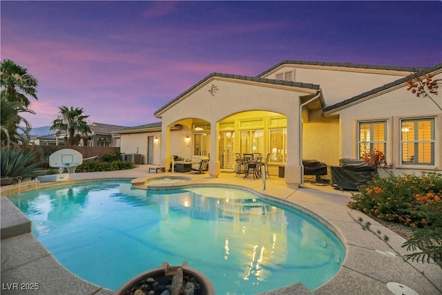 pool at dusk with central AC, a patio area, and an in ground hot tub