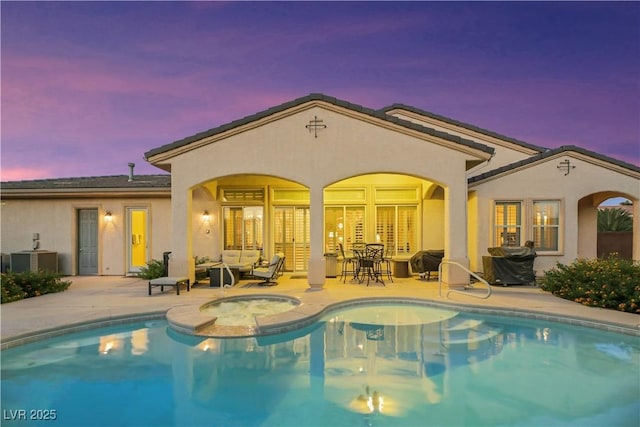 back house at dusk with a patio, central AC unit, and a pool with hot tub