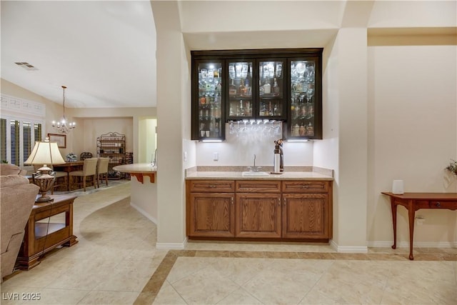 bar featuring pendant lighting, an inviting chandelier, vaulted ceiling, and sink