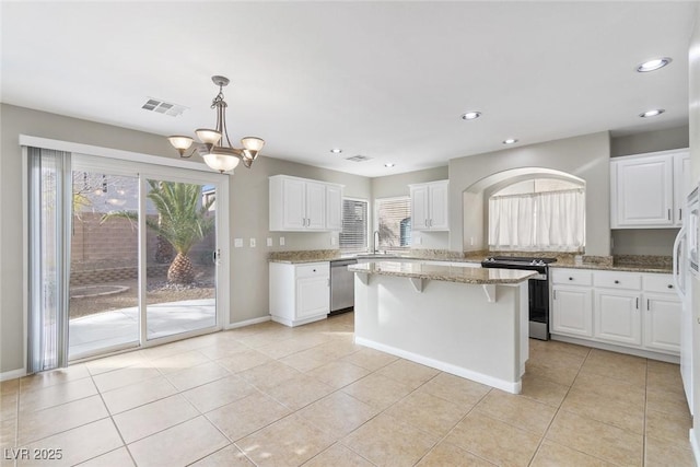 kitchen featuring white cabinetry, light stone counters, decorative light fixtures, appliances with stainless steel finishes, and a kitchen island