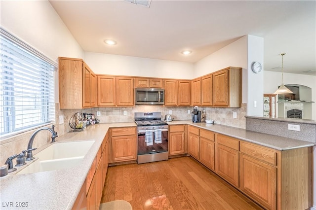 kitchen with sink, tasteful backsplash, hanging light fixtures, light wood-type flooring, and appliances with stainless steel finishes