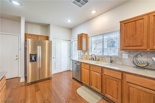 kitchen featuring tasteful backsplash, stainless steel appliances, sink, and light hardwood / wood-style flooring