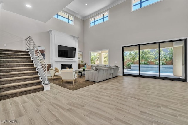 living room with a towering ceiling, ornamental molding, and light hardwood / wood-style floors