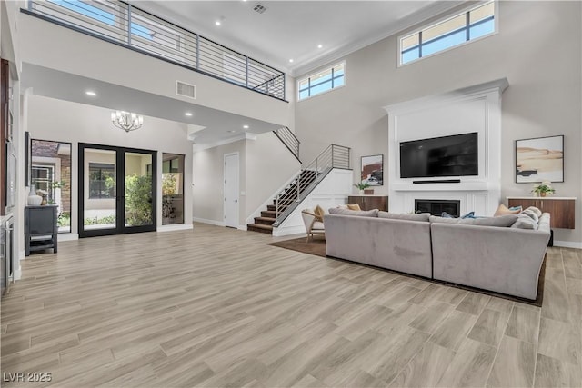 living room with a towering ceiling, light hardwood / wood-style flooring, a chandelier, ornamental molding, and french doors