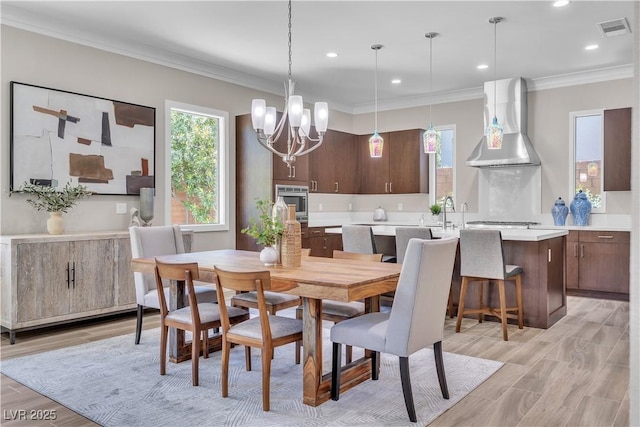 dining space with crown molding, a notable chandelier, and light wood-type flooring