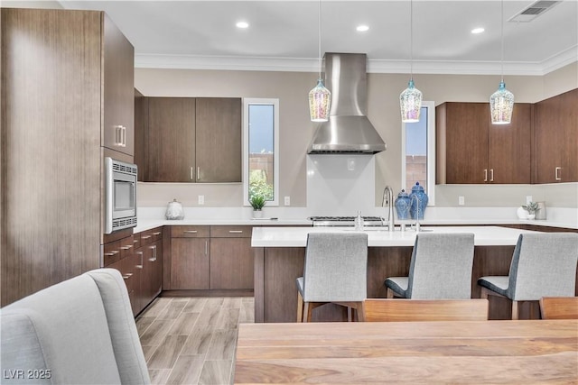 kitchen with hanging light fixtures, a breakfast bar, wall chimney range hood, and stainless steel microwave