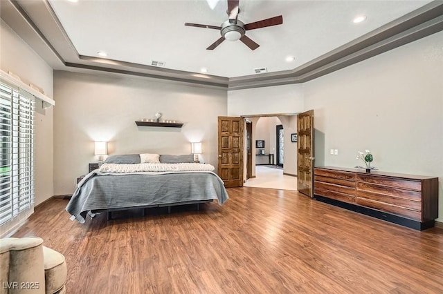 bedroom with wood-type flooring, ceiling fan, and a tray ceiling