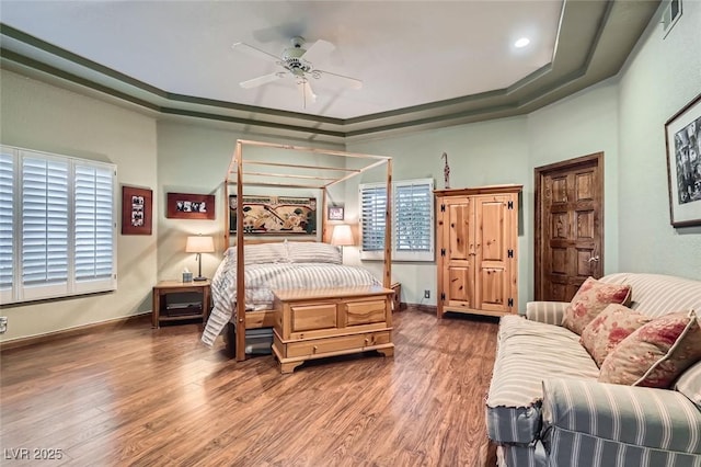 bedroom with hardwood / wood-style flooring, a raised ceiling, and ceiling fan