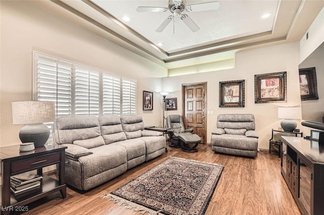 living room with a raised ceiling, ceiling fan, and light wood-type flooring