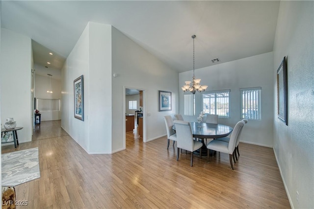 dining room with an inviting chandelier, high vaulted ceiling, and light wood-type flooring