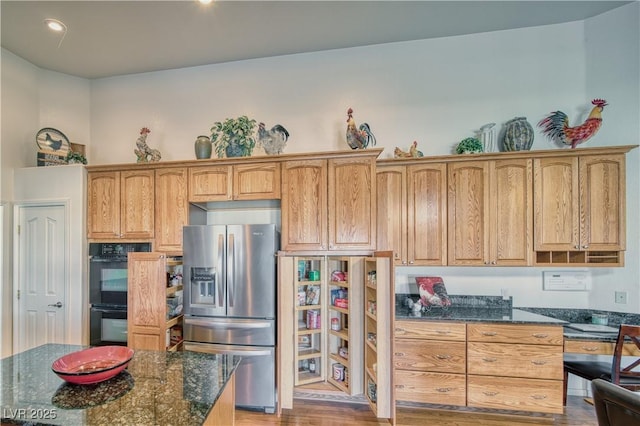 kitchen featuring double oven, dark stone counters, light hardwood / wood-style floors, and stainless steel fridge with ice dispenser