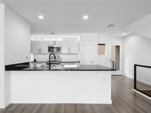 kitchen with white cabinetry, kitchen peninsula, sink, and wood-type flooring