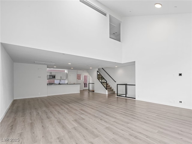 unfurnished living room featuring a high ceiling and light hardwood / wood-style flooring