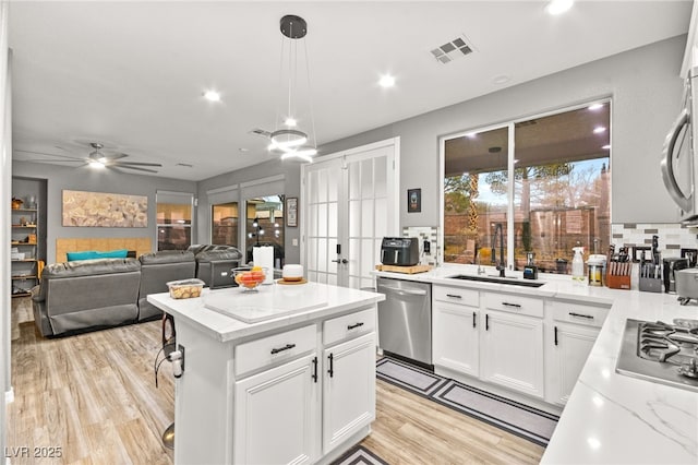 kitchen with white cabinetry, sink, light hardwood / wood-style floors, stainless steel appliances, and light stone countertops