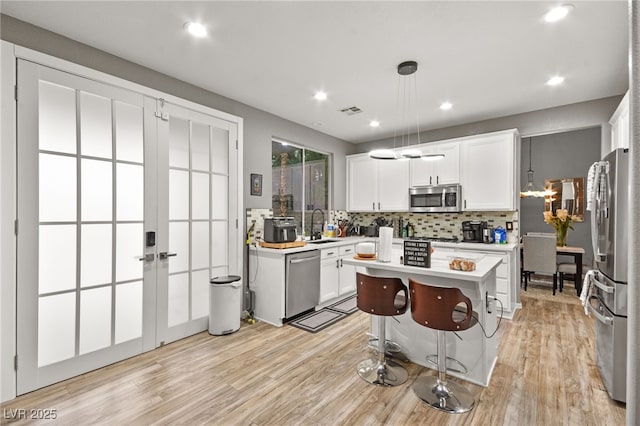 kitchen featuring white cabinetry, hanging light fixtures, stainless steel appliances, and a center island