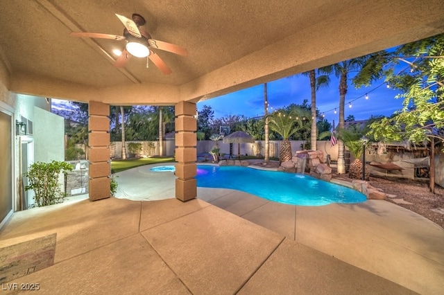 pool at dusk with pool water feature, ceiling fan, and a patio