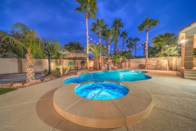 pool at dusk with a patio area and an in ground hot tub