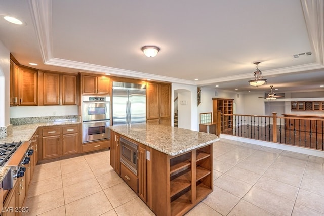 kitchen with light tile patterned floors, a center island, built in appliances, a tray ceiling, and ornamental molding