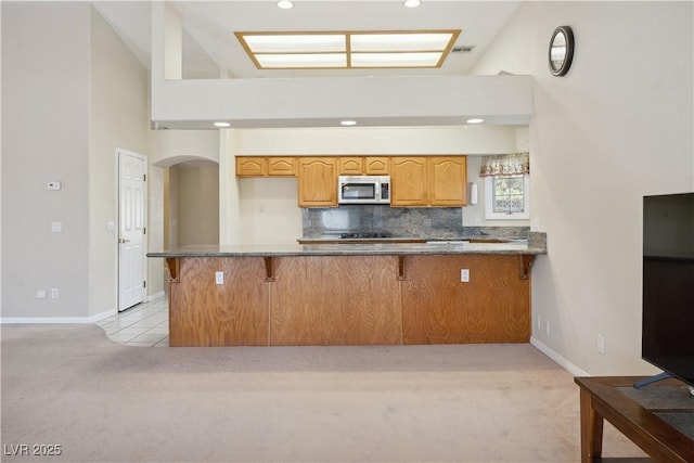 kitchen with backsplash, light colored carpet, kitchen peninsula, and a breakfast bar