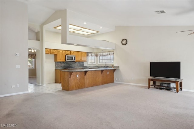 kitchen featuring lofted ceiling, light colored carpet, kitchen peninsula, and a breakfast bar