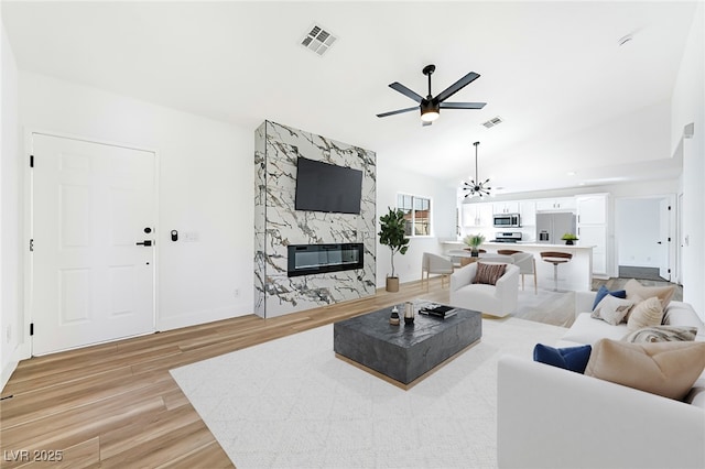 living room featuring ceiling fan with notable chandelier, light hardwood / wood-style flooring, a premium fireplace, and vaulted ceiling