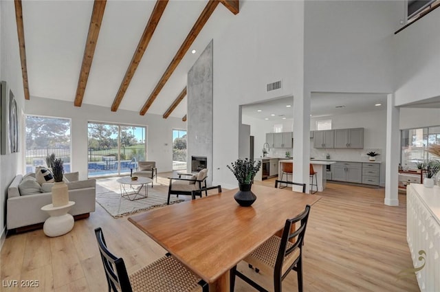 dining room with high vaulted ceiling, a fireplace, light hardwood / wood-style floors, and beamed ceiling