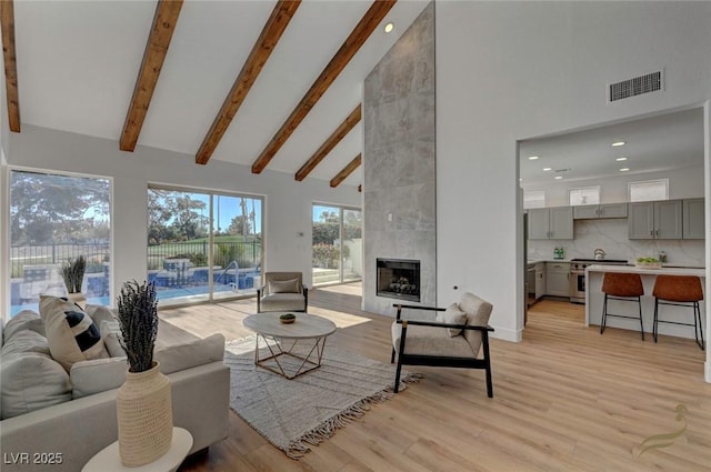 living room with beamed ceiling, high vaulted ceiling, a tile fireplace, and light hardwood / wood-style flooring