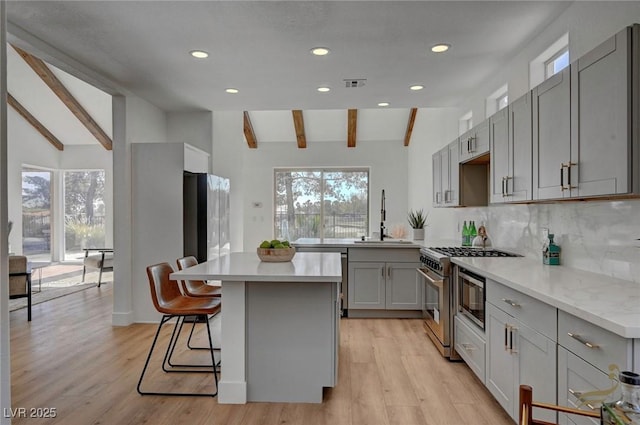 kitchen featuring sink, vaulted ceiling with beams, gray cabinetry, high end stainless steel range oven, and decorative backsplash