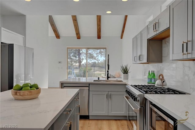 kitchen with gray cabinetry, backsplash, light stone countertops, and appliances with stainless steel finishes