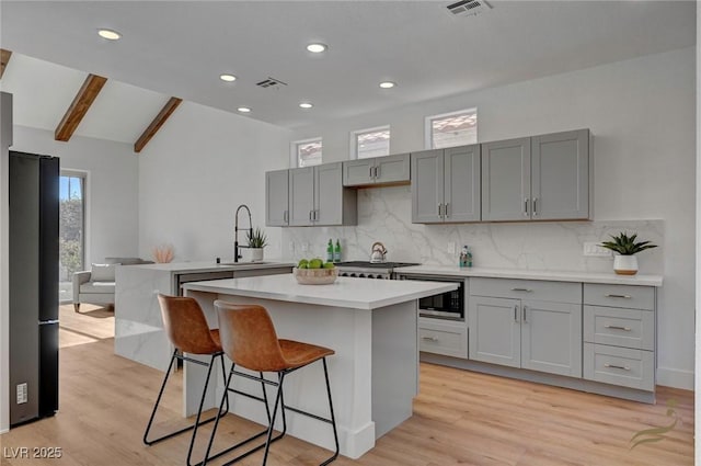 kitchen featuring gray cabinets, built in microwave, sink, a breakfast bar area, and a center island