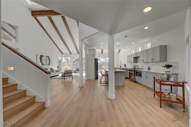 kitchen with gray cabinets, beamed ceiling, backsplash, high end stainless steel range, and light hardwood / wood-style flooring