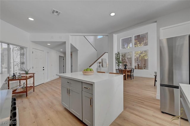 kitchen with gray cabinets, a center island, stainless steel fridge, and light hardwood / wood-style flooring