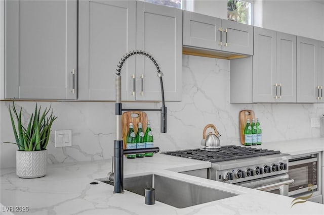 kitchen with light stone counters, decorative backsplash, gray cabinets, and stainless steel appliances