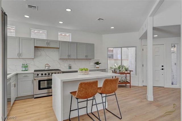 kitchen with a breakfast bar area, stainless steel gas range oven, a center island, light wood-type flooring, and backsplash