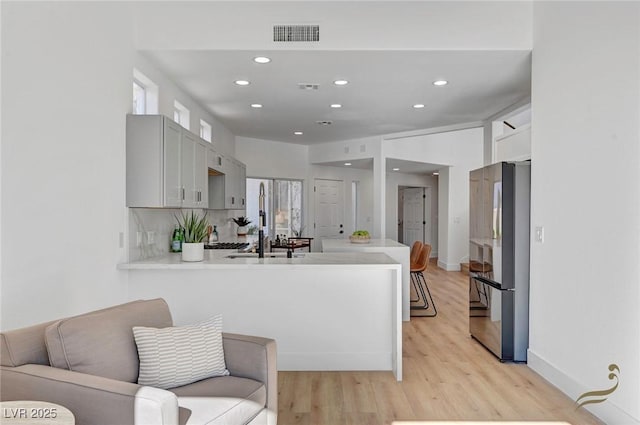 kitchen featuring stainless steel fridge, kitchen peninsula, light hardwood / wood-style flooring, and backsplash